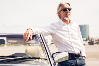 old man posing by car